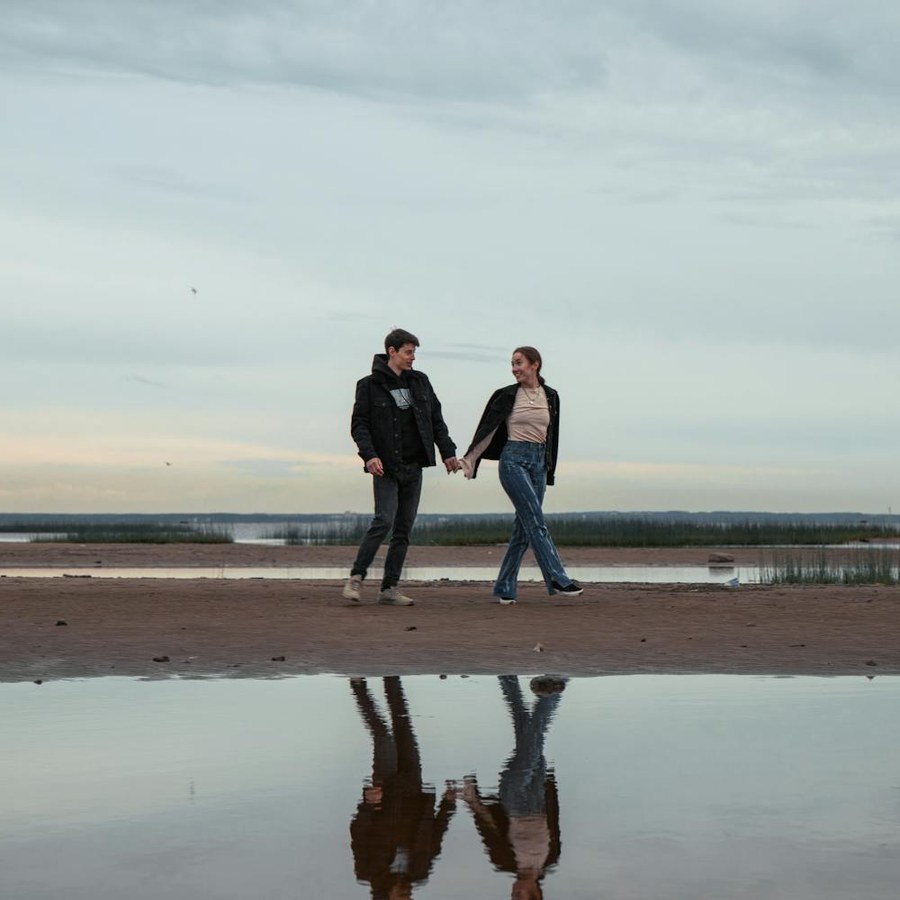 Couple seen from behind holding hands while walking along a sandy beach at sunset